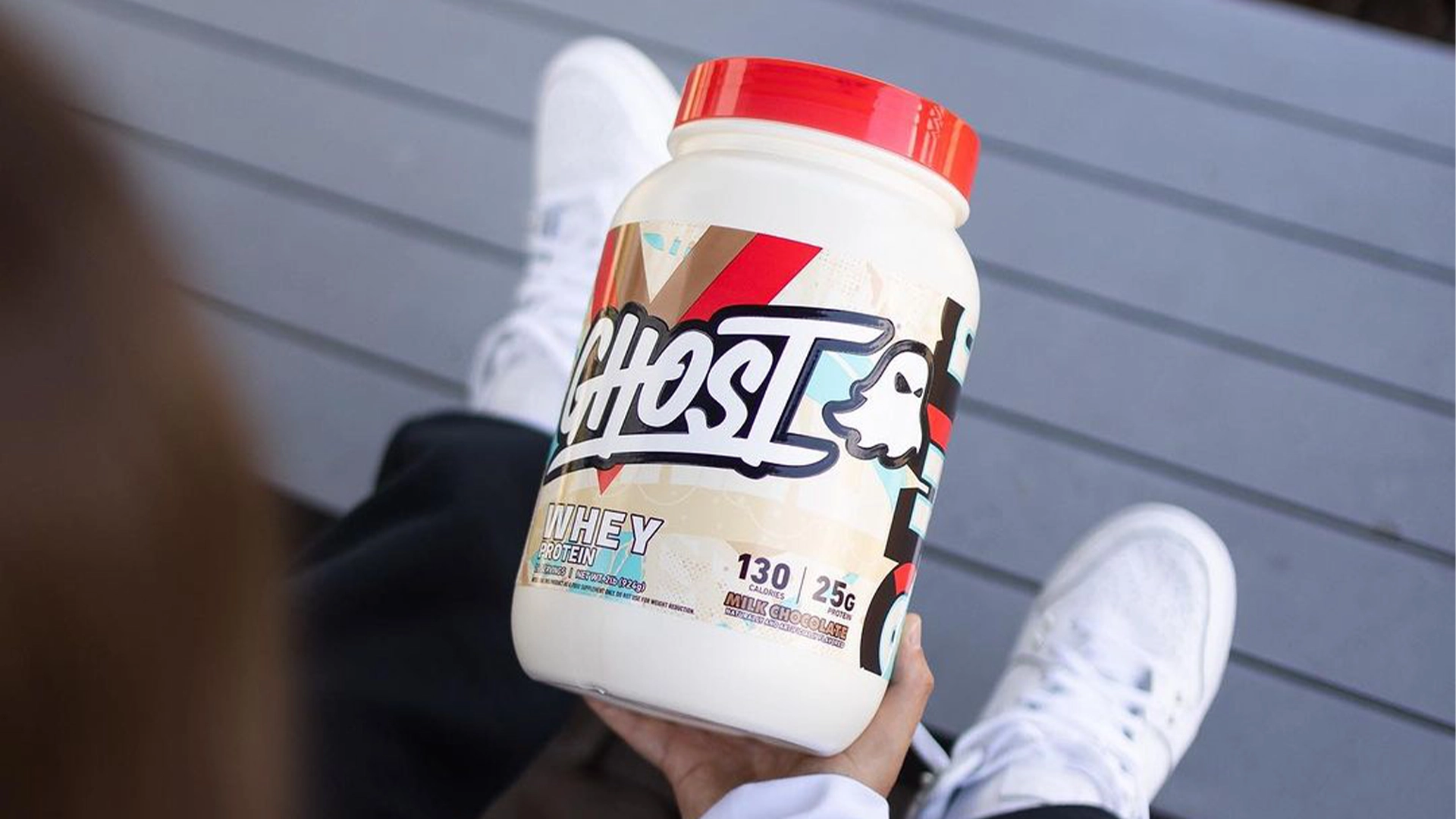 Person holding a tub of Ghost Whey 